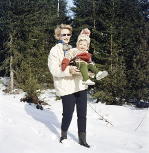 Äiti poseeraa kameralle hiihtoasussa tyttären kanssa metsän reunassa matkalla mökille Karjalohjalla. Kuva Juha Jernvall 1960, Helsingin kaupunginmuseo.