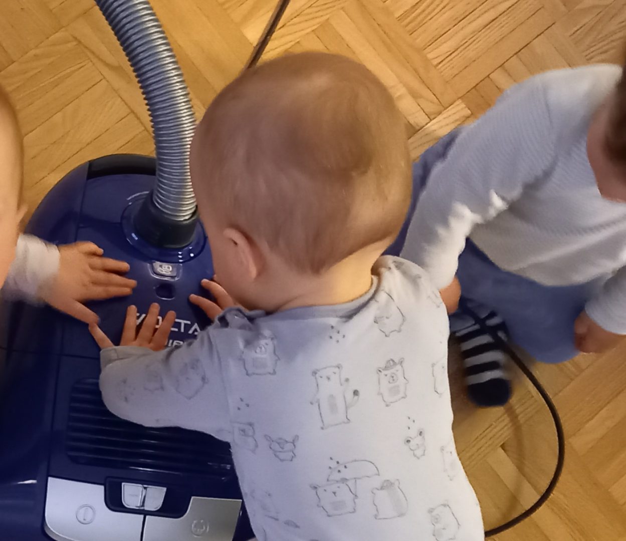 Kolme pientä lasta imurin kimpussa. Kasvot eivät näy.