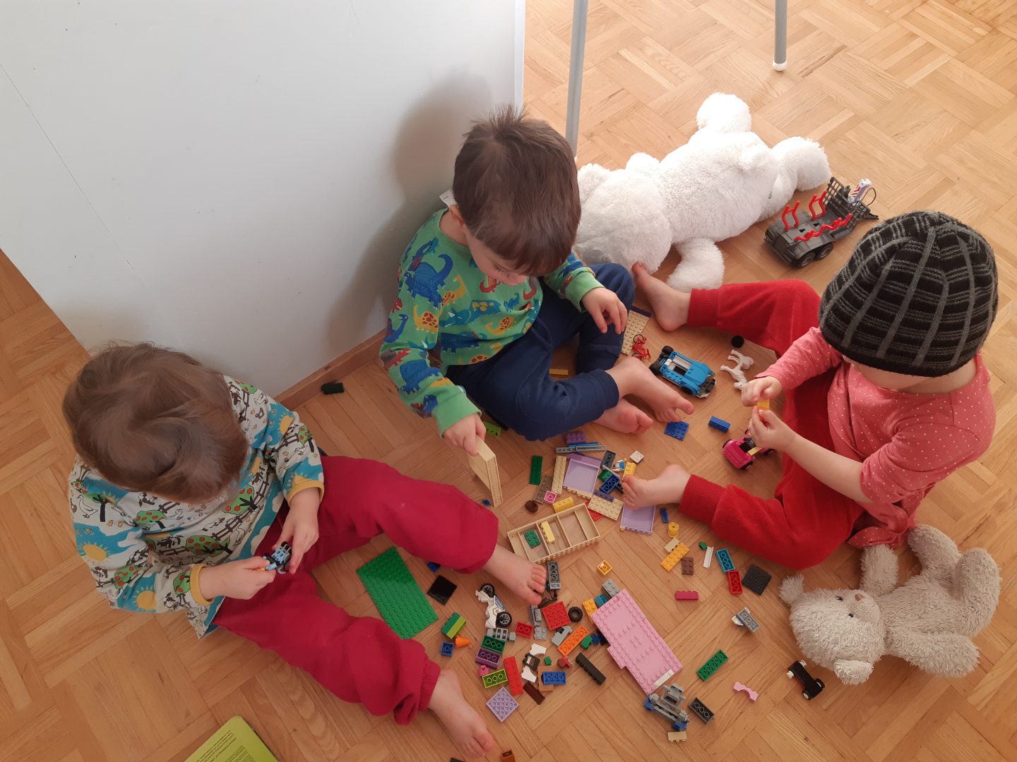 Kolme lasta ylhäältäpäin kuvattuna leikkimässä Legoilla.