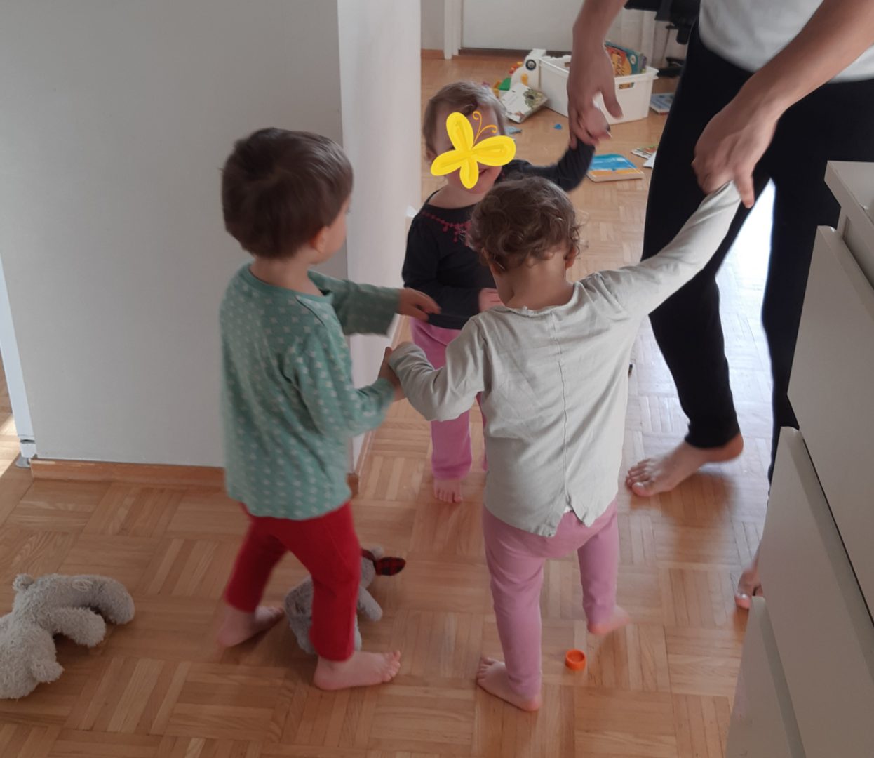 Kolme lasta tanssii käsi kädessä, isän kädet näkyvät myös.