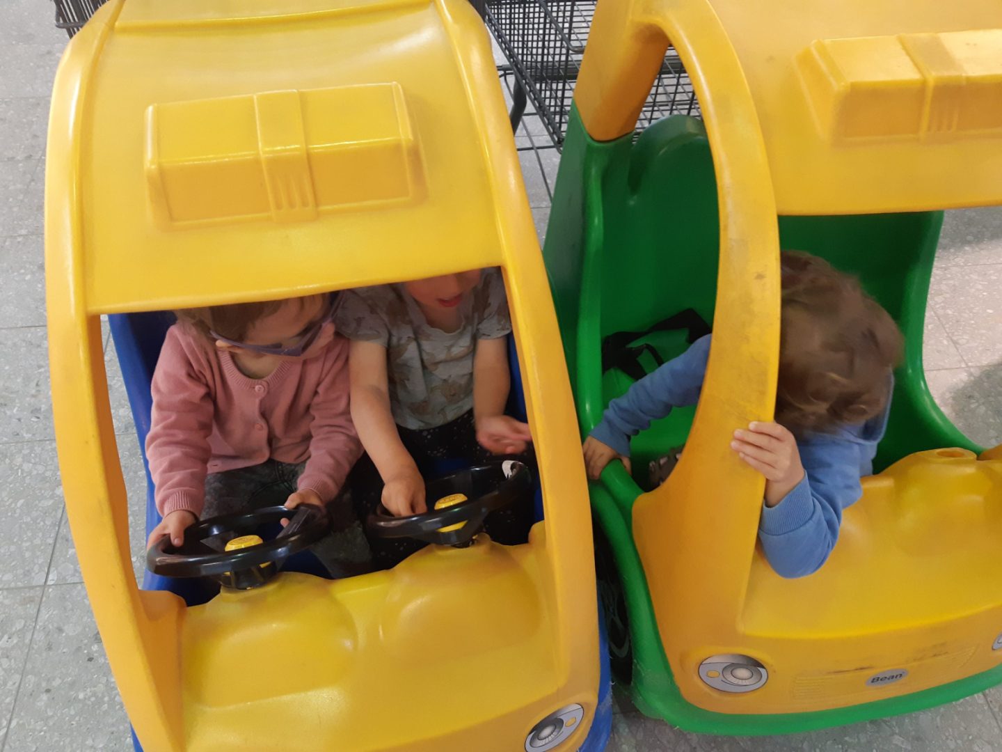 Kolme lasta ostoskeskuksen autokärryssä.