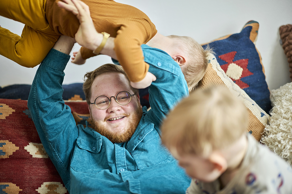 Vauhdikkaassa kuvassa keskellä on hymyilevä keski-ikäinen isä, joka nostaa päänsä päälle taaperoa. Samalla hän katsoo edessään leikkivää toista taaperoa.
