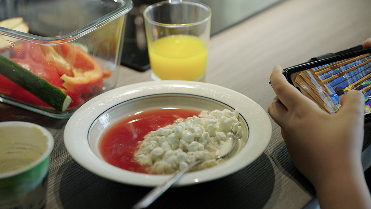 Kuva aamupalasta, jossa on mehukeittoa, raejuustoa ja tuoremehua. Lapsella on kädessään kännykkä.