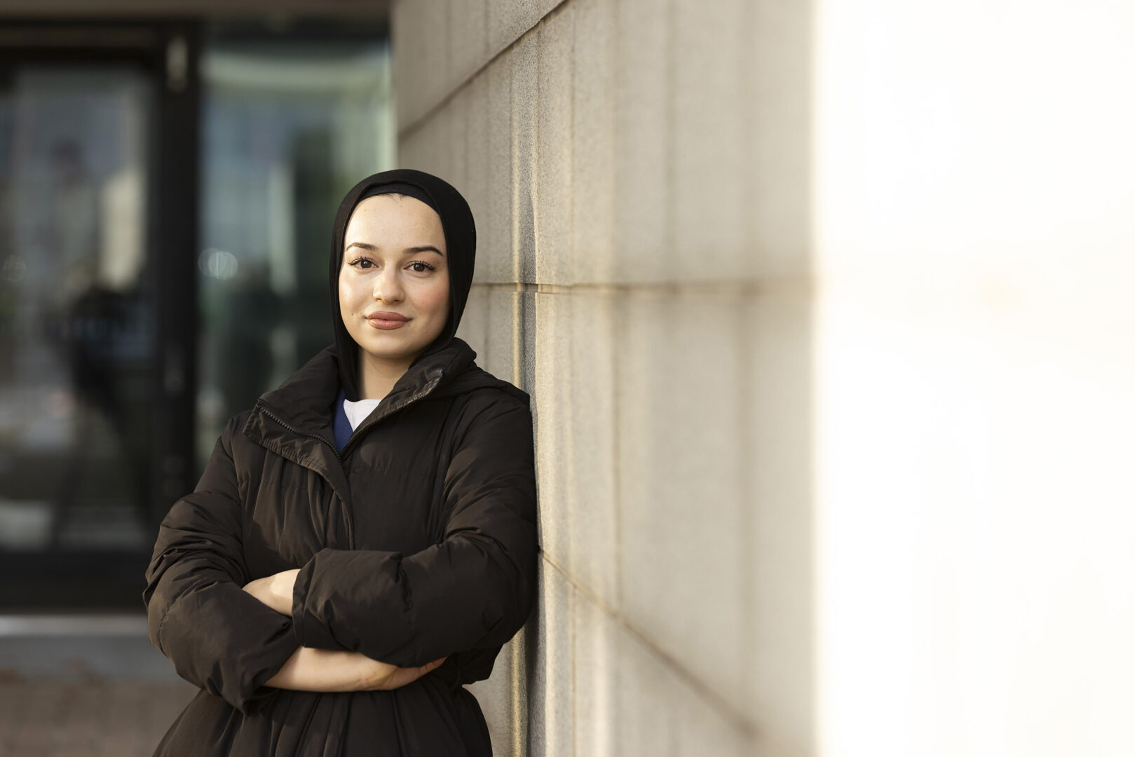 Nuori nainen nojaa rakennuksen seinää vasten ja katsoo kameraan.