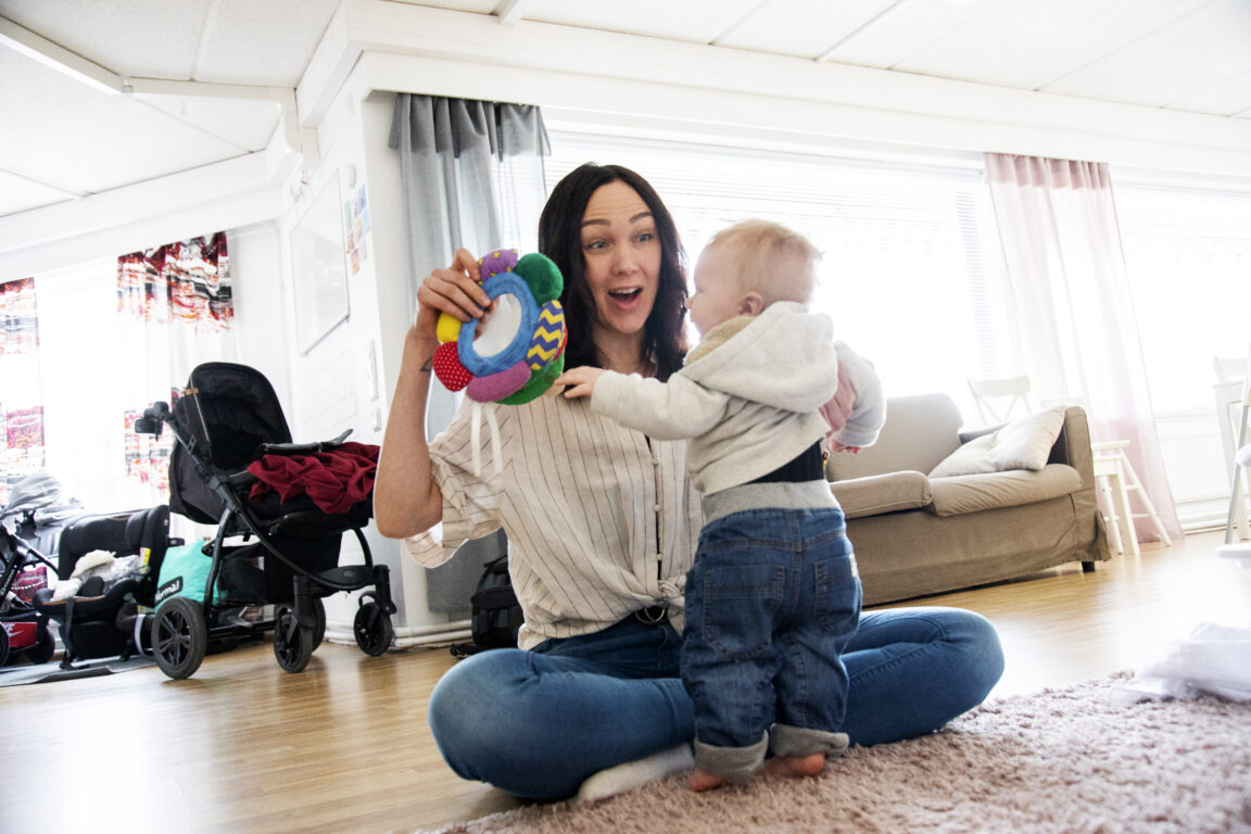 Ohjaaja leikittää sylissään pientä lasta. Taustalla näkyy kodinomainen tila.