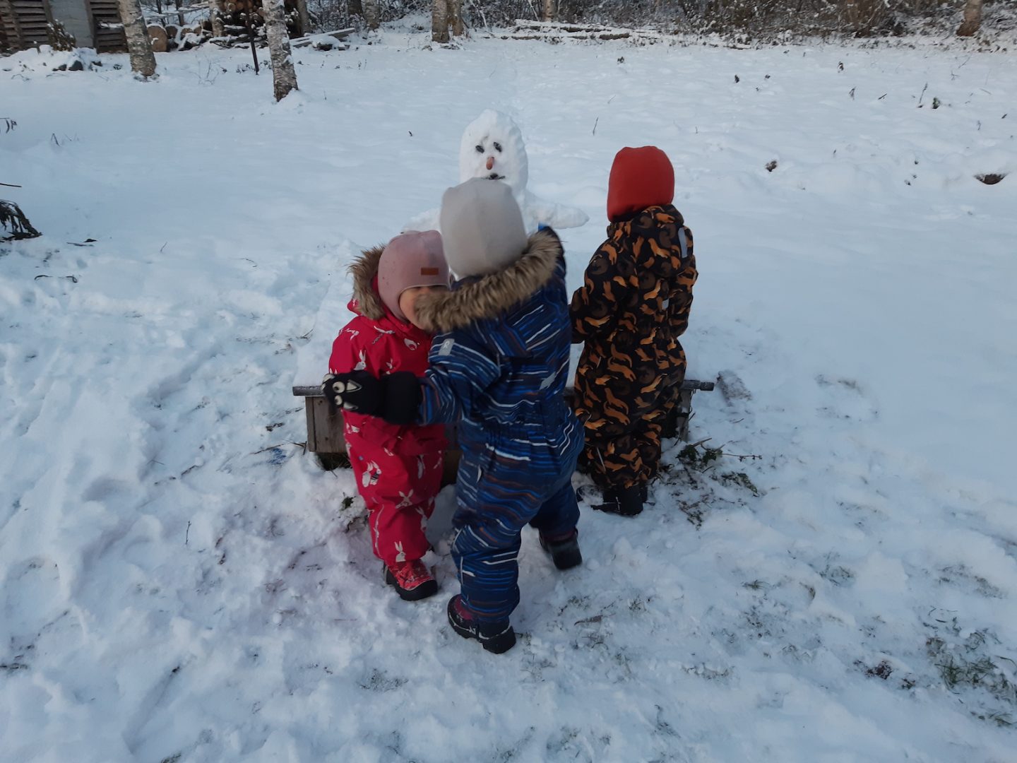 Kolme lasta lumiukon ympärillä.