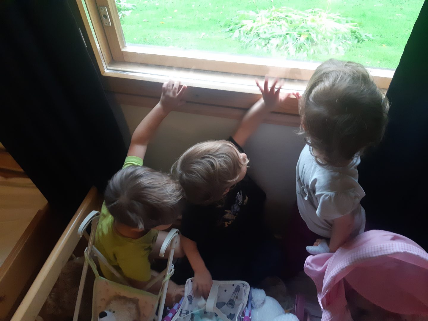 Kolme lasta istuu sängyllä nukenkärryjen kanssa.