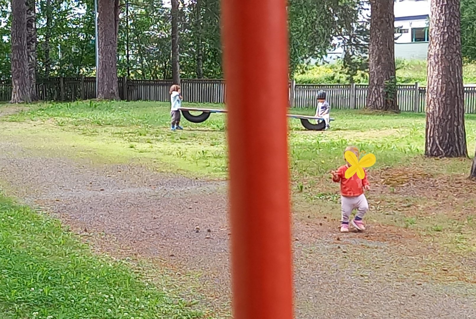 Kolme lasta leikkimässä ulkona, kaukaa kuvattu.