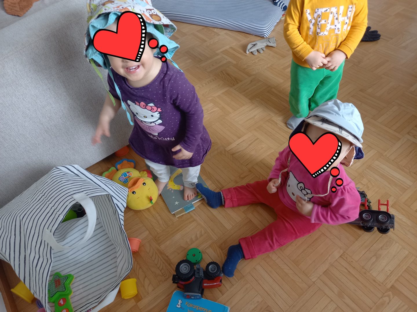 Kolme lasta lelujen keskellä, kasvot peitetty.