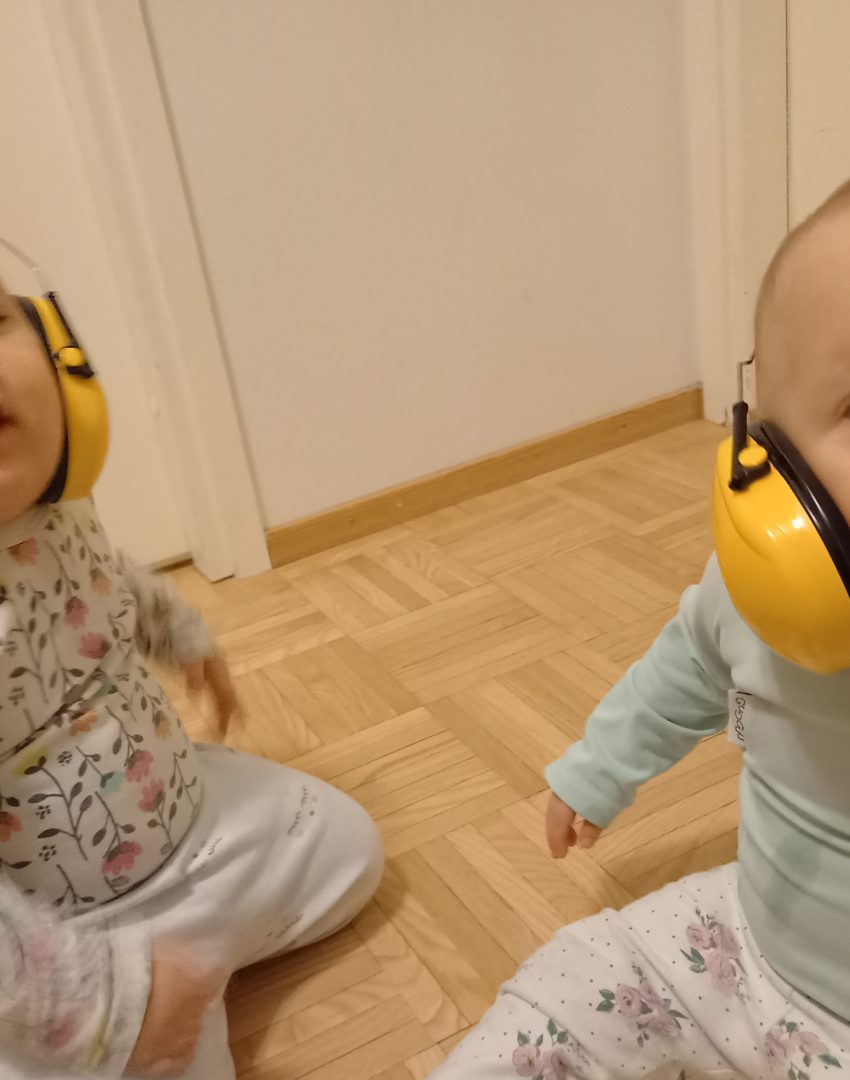 Kaksi pientä lasta, päät hieman näkyvät ja päässä kuulosuojaimet.