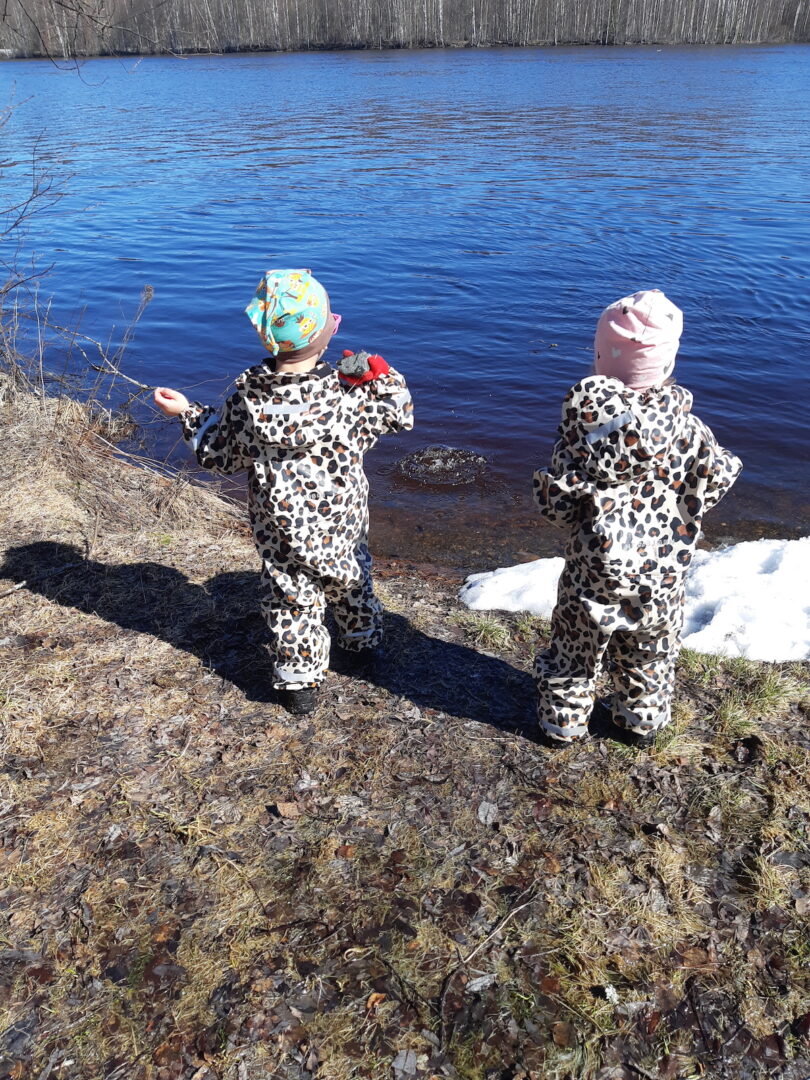 Kaksi lasta heittää kiviä rannassa.