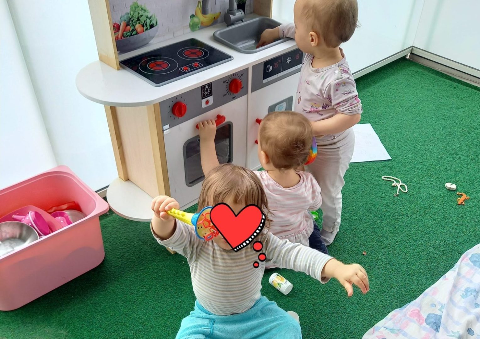 Kolme lasta leikkikeittiön äärellä, kasvot käännetty pois tai peitetty.