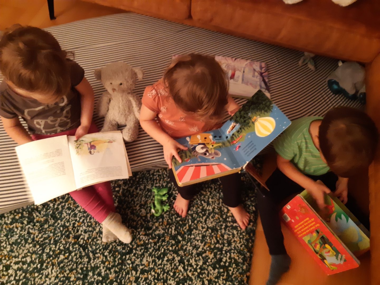 Kolme taaperoa istuu tyynyillä ja lukee kirjoja.