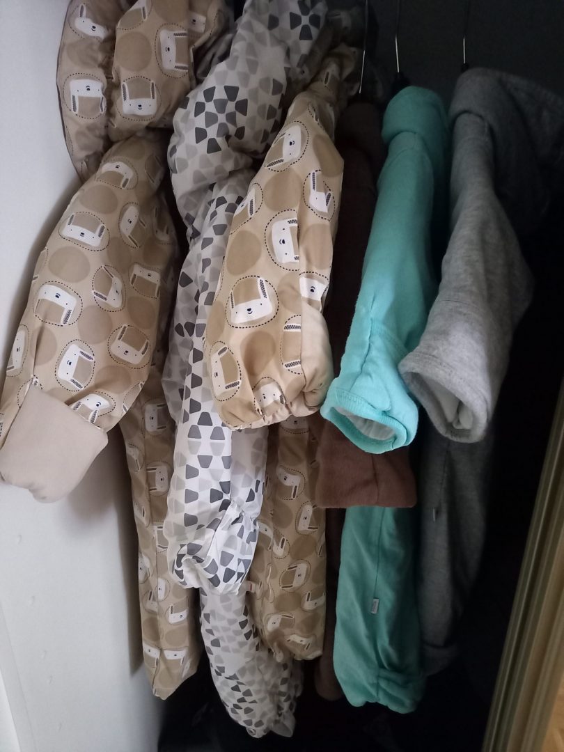 Kolme äitiyspakkauksen toppa- ja vanupukua hengareissa.
