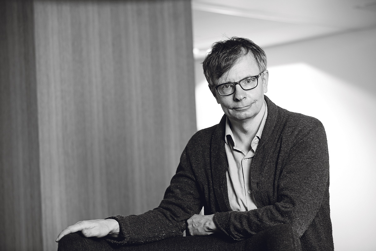 Heikki Hiilamo nojaa pöytään mustavalkoisessa kuvassa.