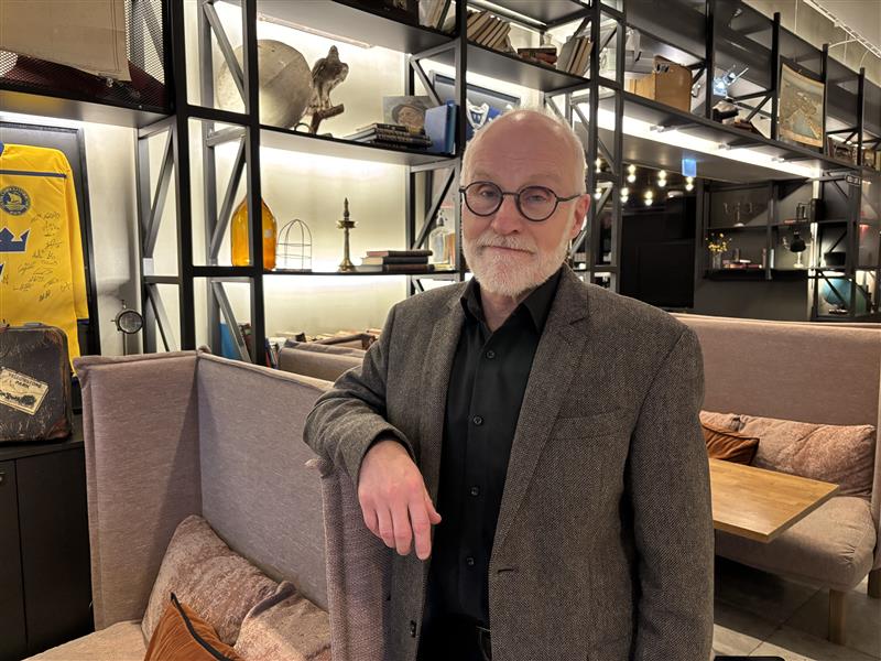 Pentti Lemmetyinen seisoo puolikuvassa. Taustalla näkyy valaistu hyllykkö.