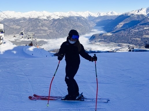 Kuva Mineasta alppimaisemissa. Hän poseeraa kameralle rinteessa alppihiihtovarusteissa.