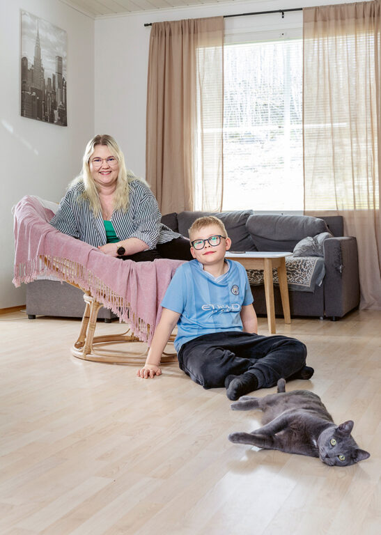 Nainen ja poika istuva olohuoneessa ja katsovat kameraan.