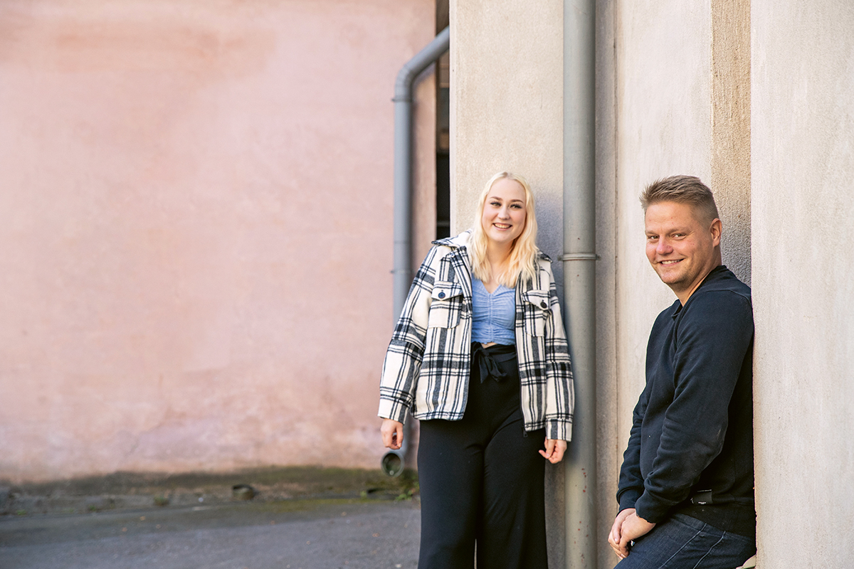 Nuori nainen ja nuori mies seisovat kuvassa nojaillen seinään.