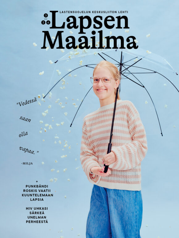 Milja seisoo studiossa sinistä taustaa vasten ja pitää läpinäkyvää sateenvarjoa kädessään. Taivaalta sataa popcorneja.