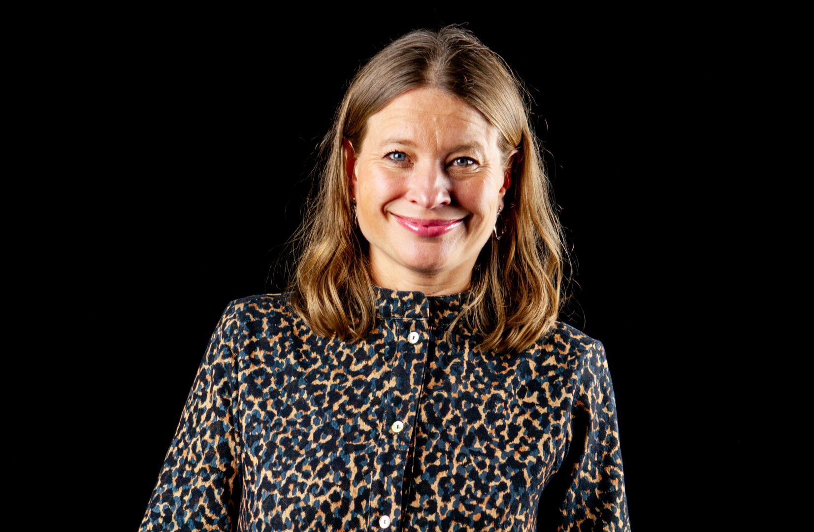 Elina Kiiski-Kataja hymyilee studiossa otetussa lähikuvassa. Tausta on musta.