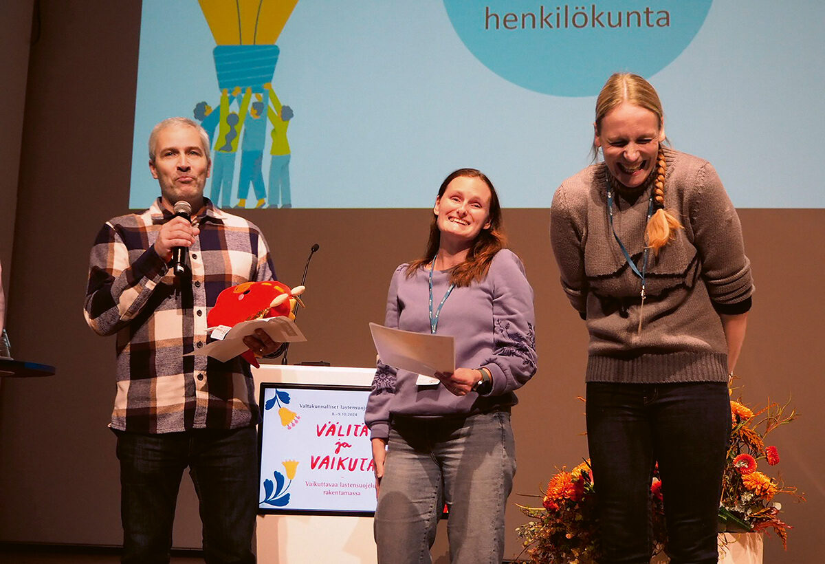 Kolme henkilöä Valtakunnallisten lastensuojelupäivien lavalla vastaanottamassa palkintoa.