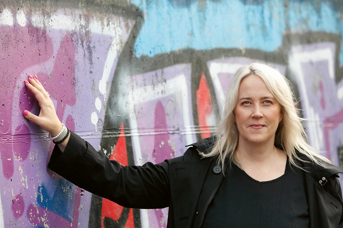 Vaalea- ja pitkätukkainen nainen seisoo graffitimuurin edessä.