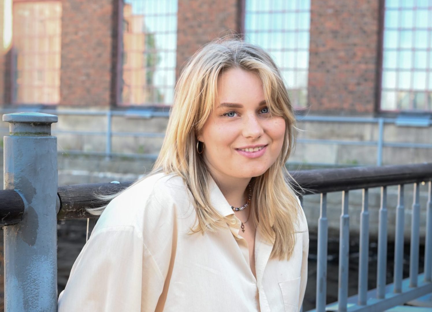 Riina Tanskanen istuu ja nojaa metalliseen aitaan rakennuksen edessä.