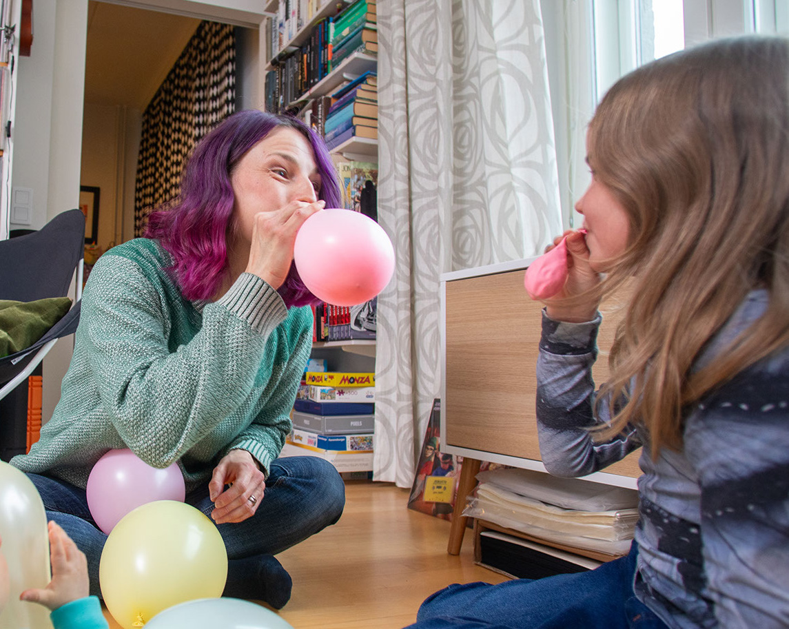Nainen ja vanhempi lapsi leikkivät ilmapalloilla vauvan edessä.