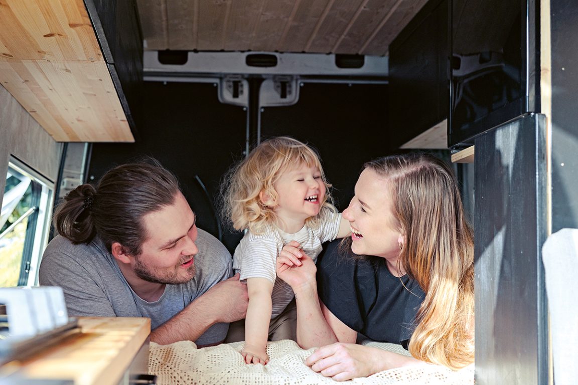 Sulo nauraa iloisena vanhempiensa välissä pakettiautoon rakennetulla sängyllä. 