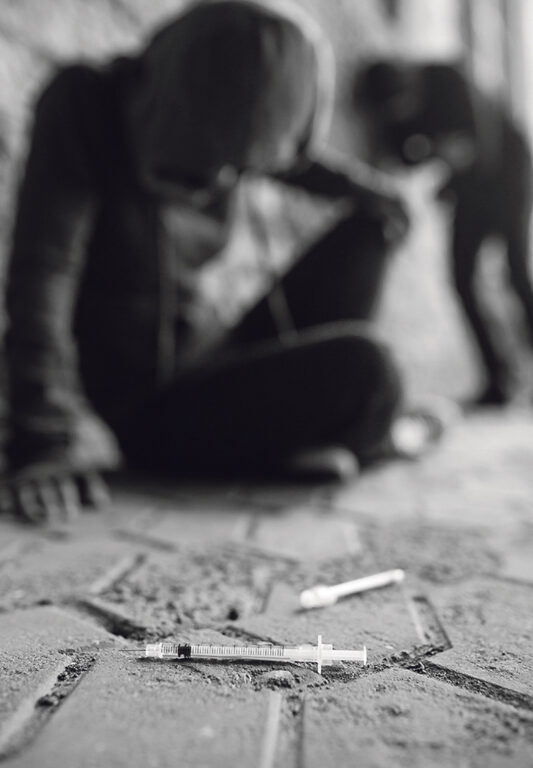 Nuori istuu kadulla vieressään käytettyjä huumeruiskuja.