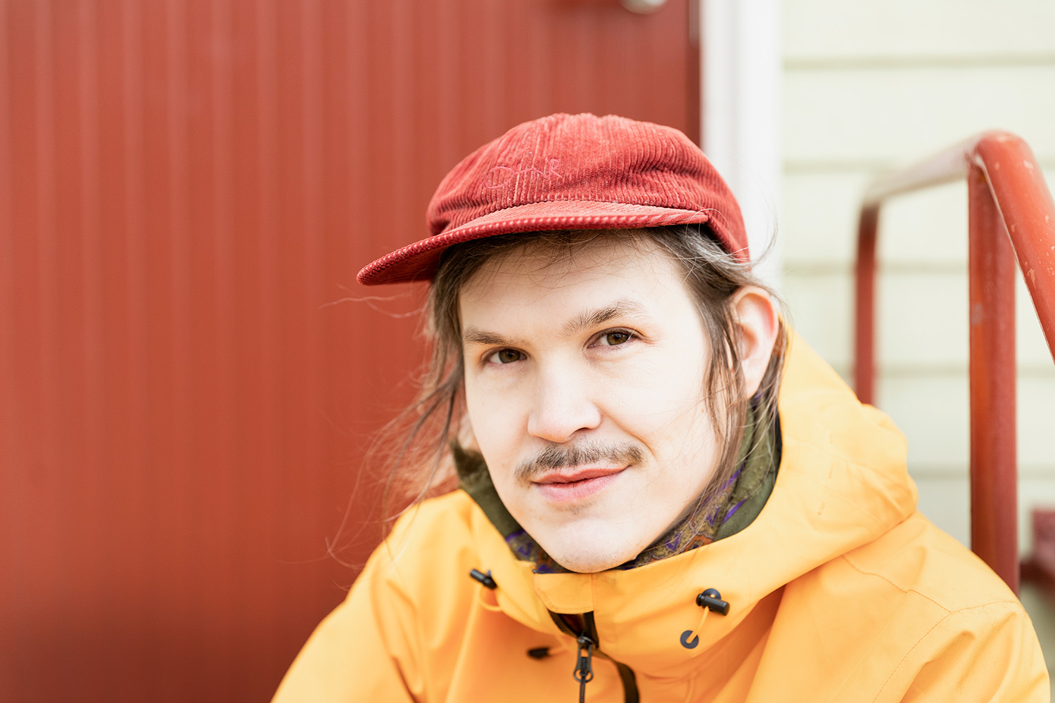 Keltatakkinen, lippalakkipäinen Joonatan Tola läheltä kuvattuna oven edessä portailla.