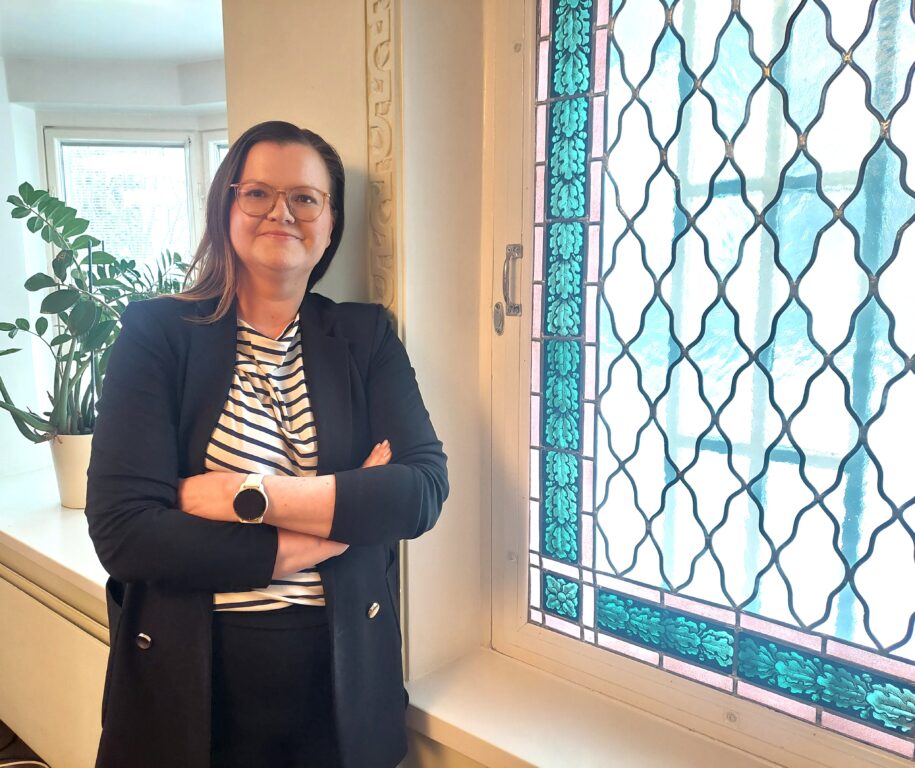 Valokuva Laura Nilasta, joka seisoo värikkään ikkunalasin vieressä.