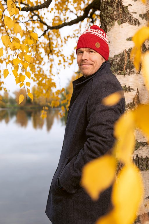 Mies punainen pipo päässä seisoo syksyisten puiden katveessa. Markus Hirvonen. 