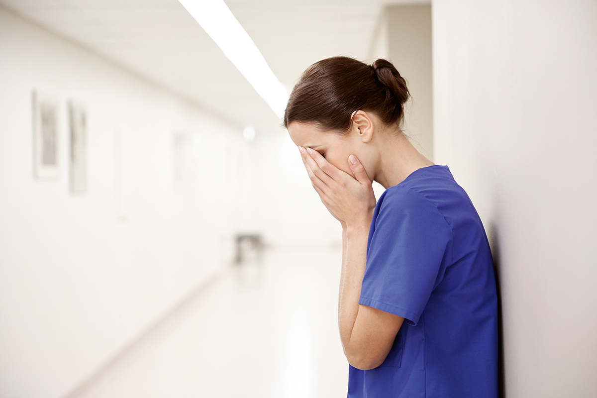 people, medicine, healthcare and sorrow concept - sad or crying female nurse at hospital corridor