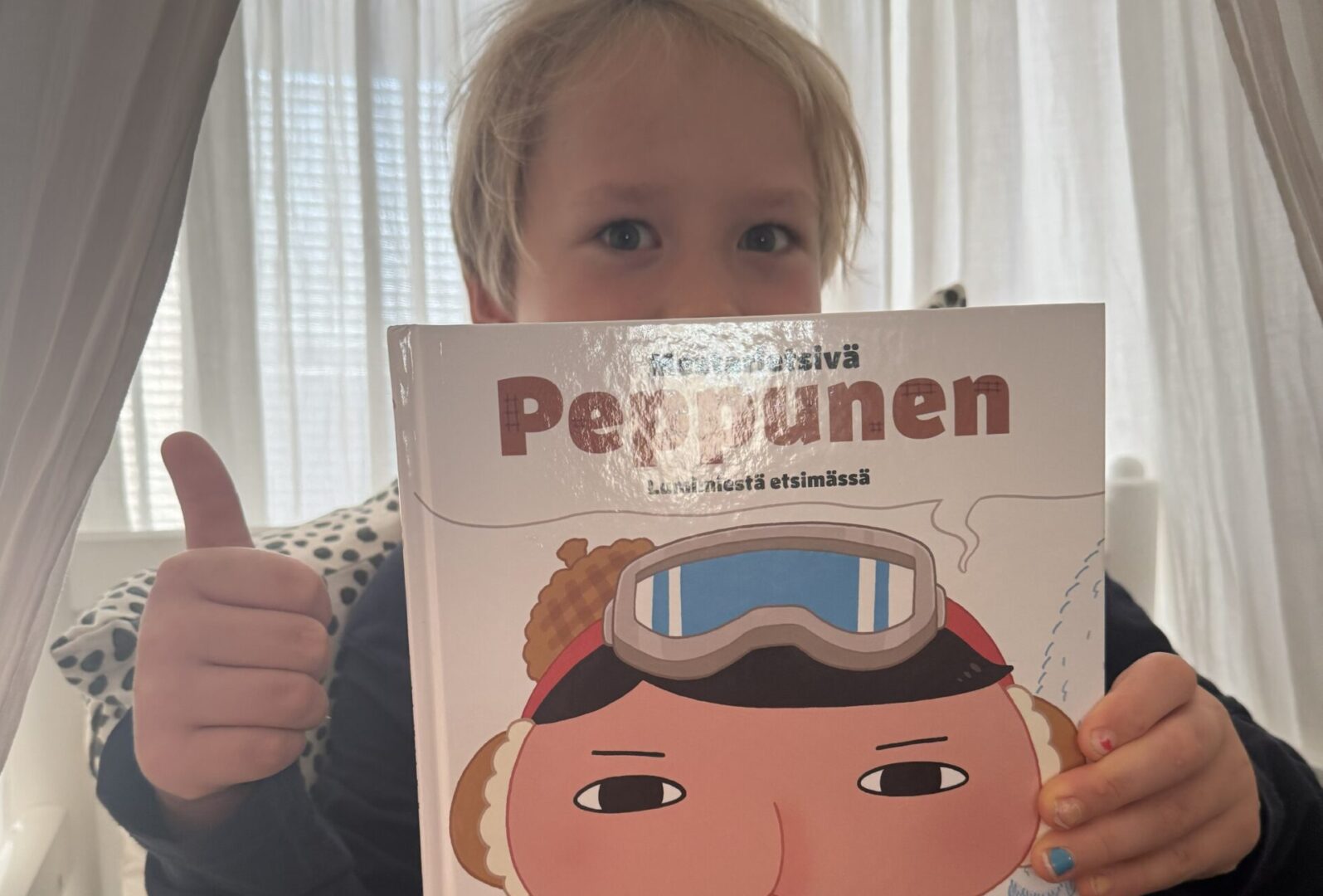 Lapsi pitelee kasvojensa edessä Peppunen kirjaa ja näyttää yläpeukkua.