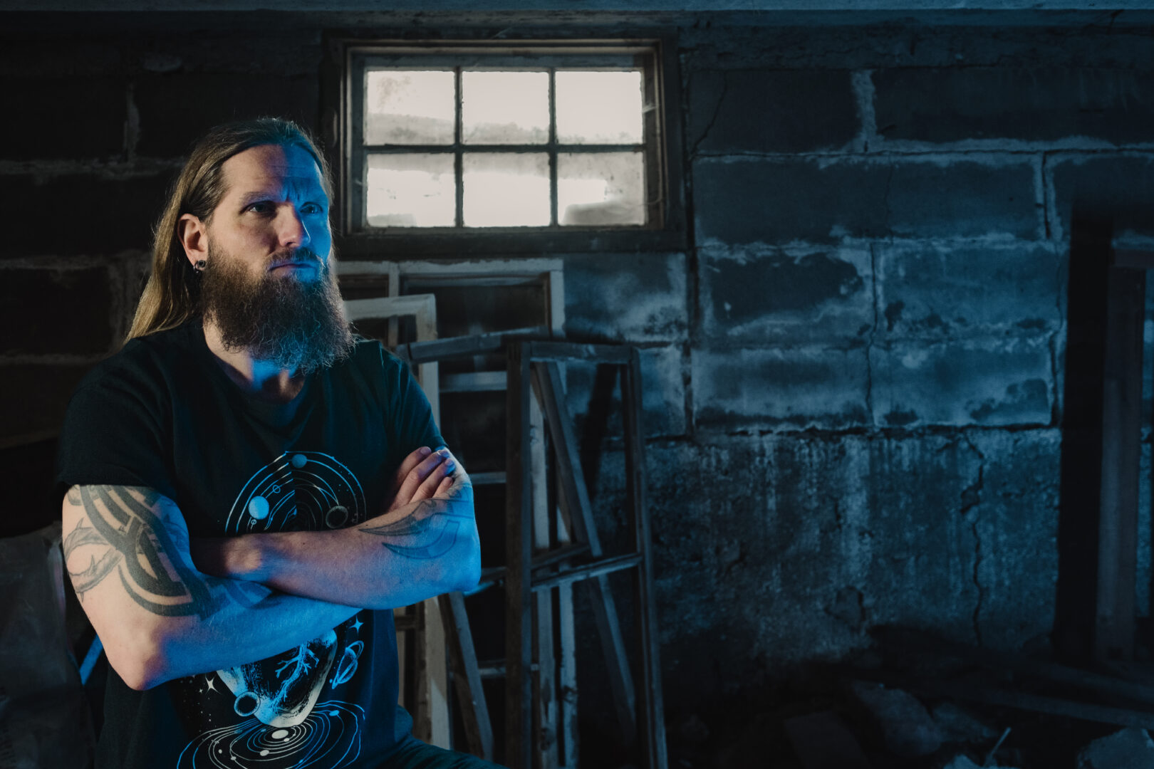 Jani Sinokki seisoo tummasävyisessä tilassa, jonka takaosassa on ikkuna.