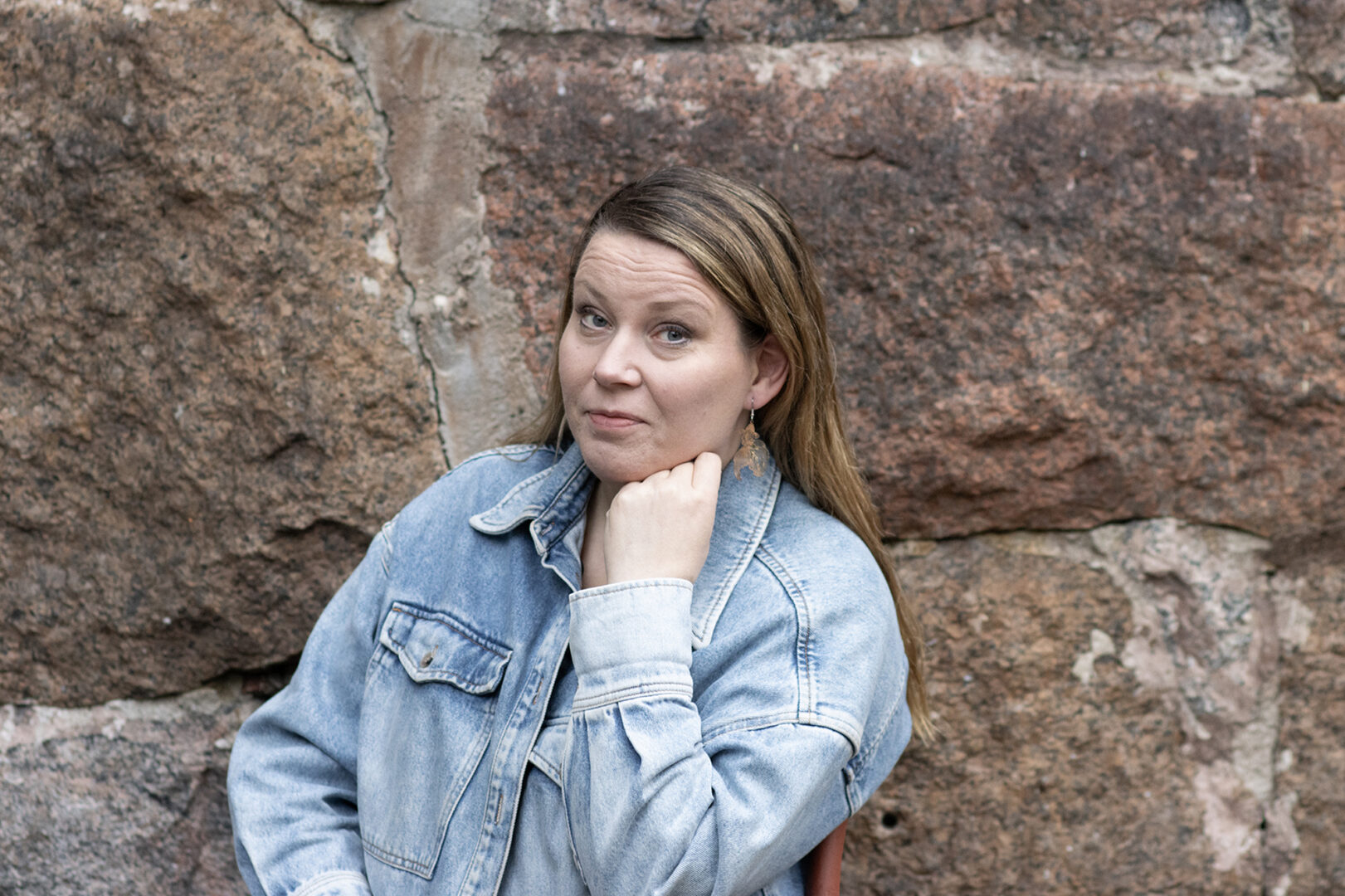 Anna Ruohonen nojaa käteensä ja katsoo kameraan. Taustalla on kivimuuri.