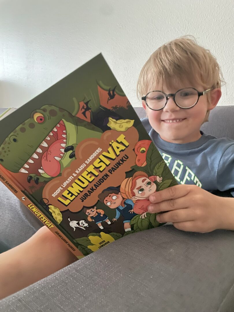 5-vuotias poika lukee kirjaa ja virnistää iloisesti.