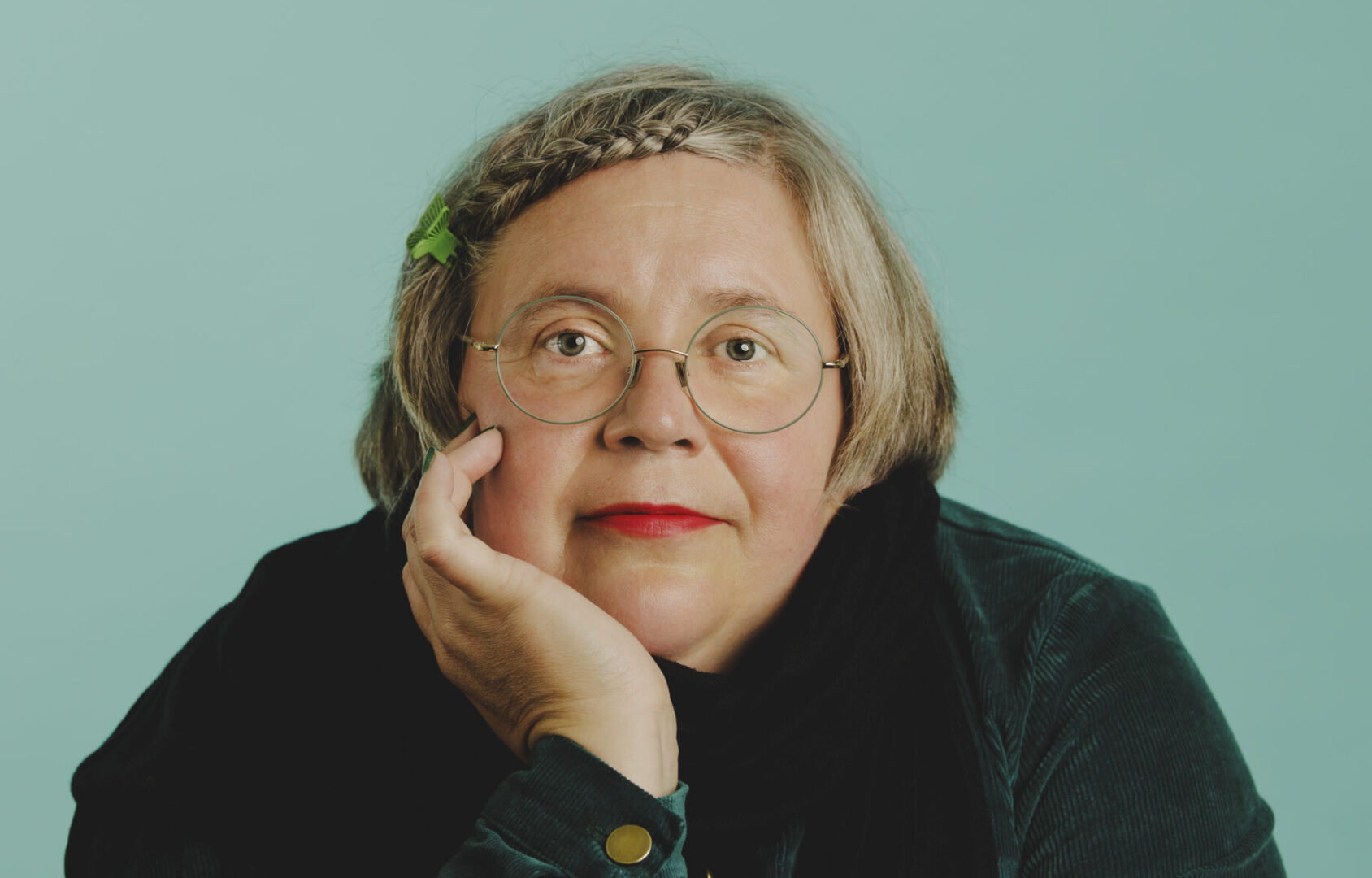 Studiokuva Elina Viinamäestä, joka nojailee käteensä ja katsoo kameraan. Hän on keski-ikäinen, ja hänellä on vaaleat lyhyet hiukset.