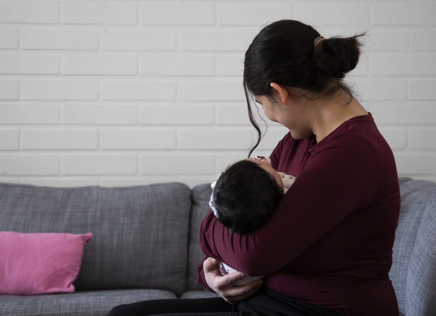 Nuori nainen istuu selin kameraan ja pitää sylissään pientä vauvaa.