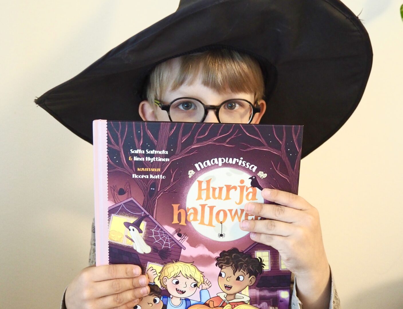 Lapsi pitää kasvojensa edessä Hurja halloween -kirjaa. Päässään hänellä on noitahattu.
