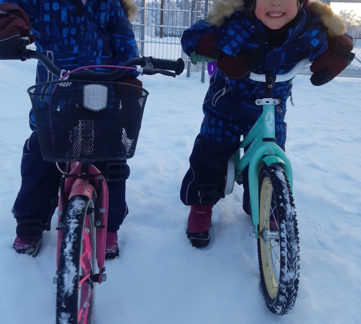 Kaksi lasta pyörien päällä talvimaisemassa.