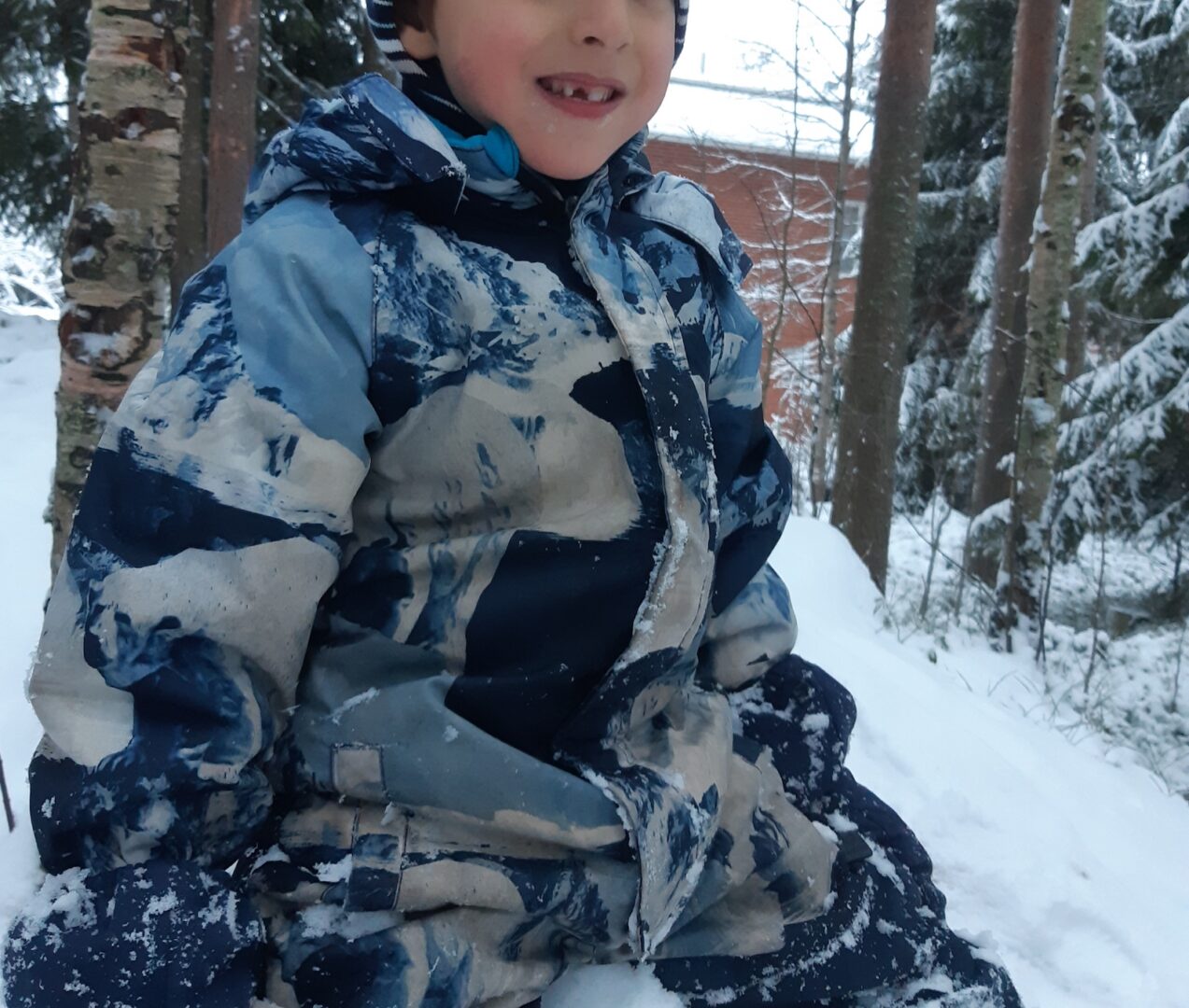 Lapsi istuu lumikasassa, yksi etuhammas irronnut.