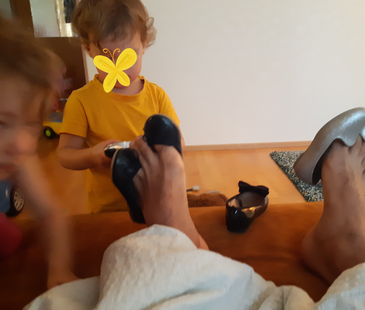 Lapsi laittaa lasten kenkiä isän varpaisiin roikkumaan.