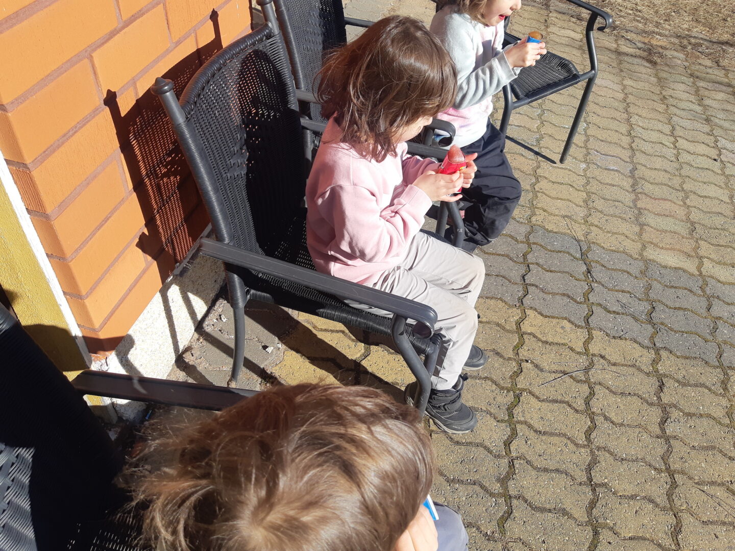 Kolme lasta puutarhatuoleissa syömässä mehujäätä.