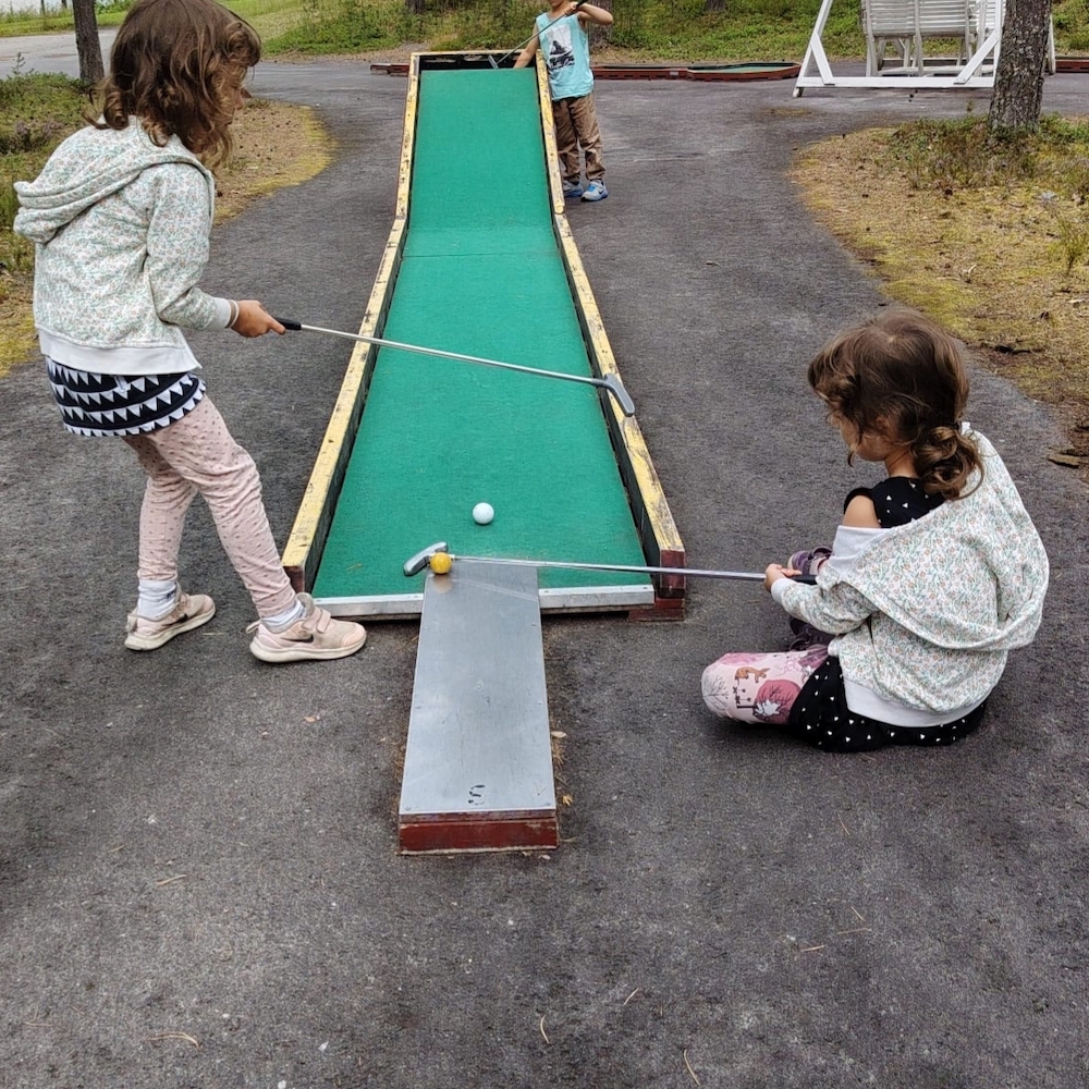 Kolmoset pelaamassa minigolfia.