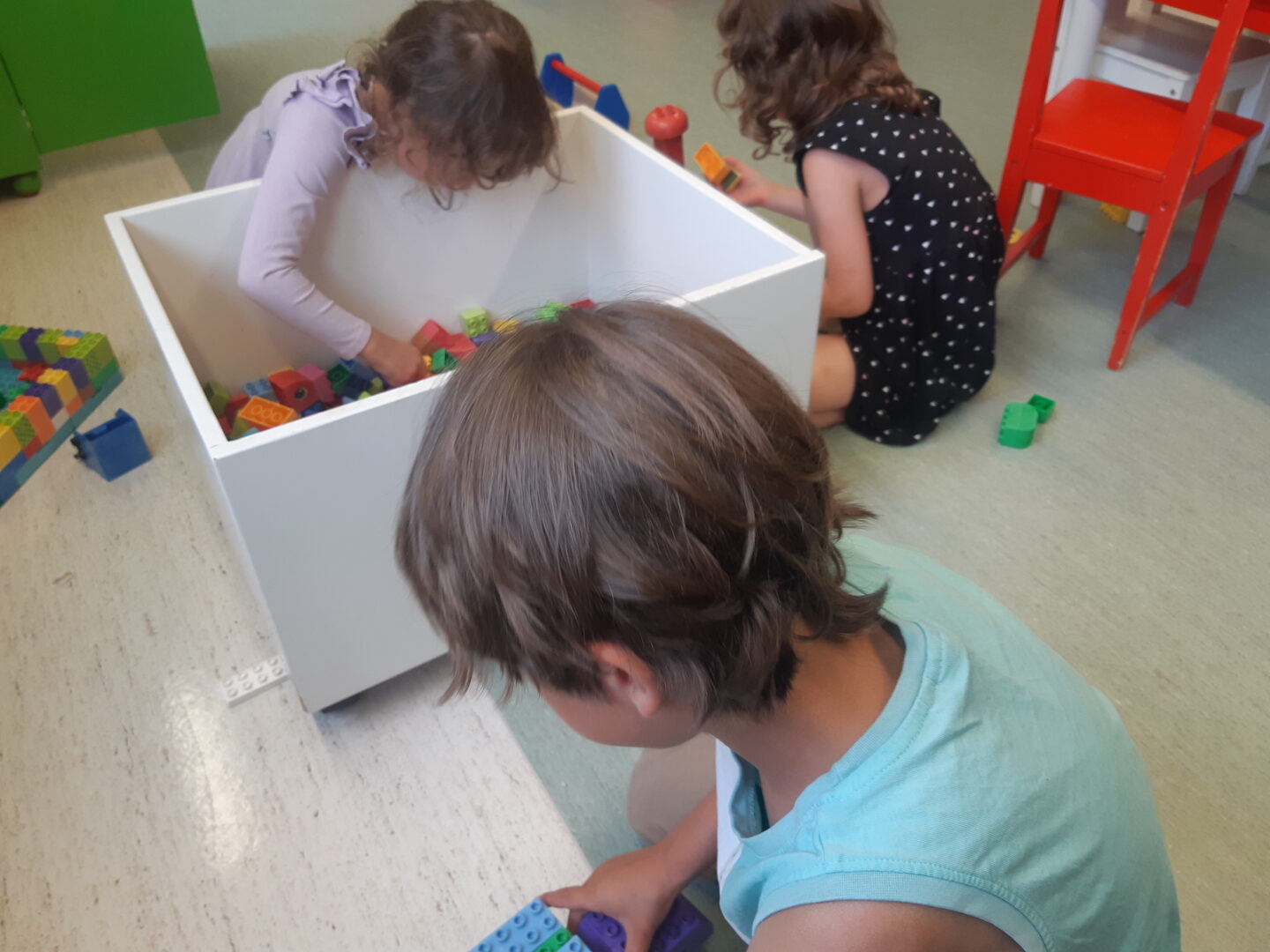 Kolme lasta leikkii Duplo-laatikon äärellä.