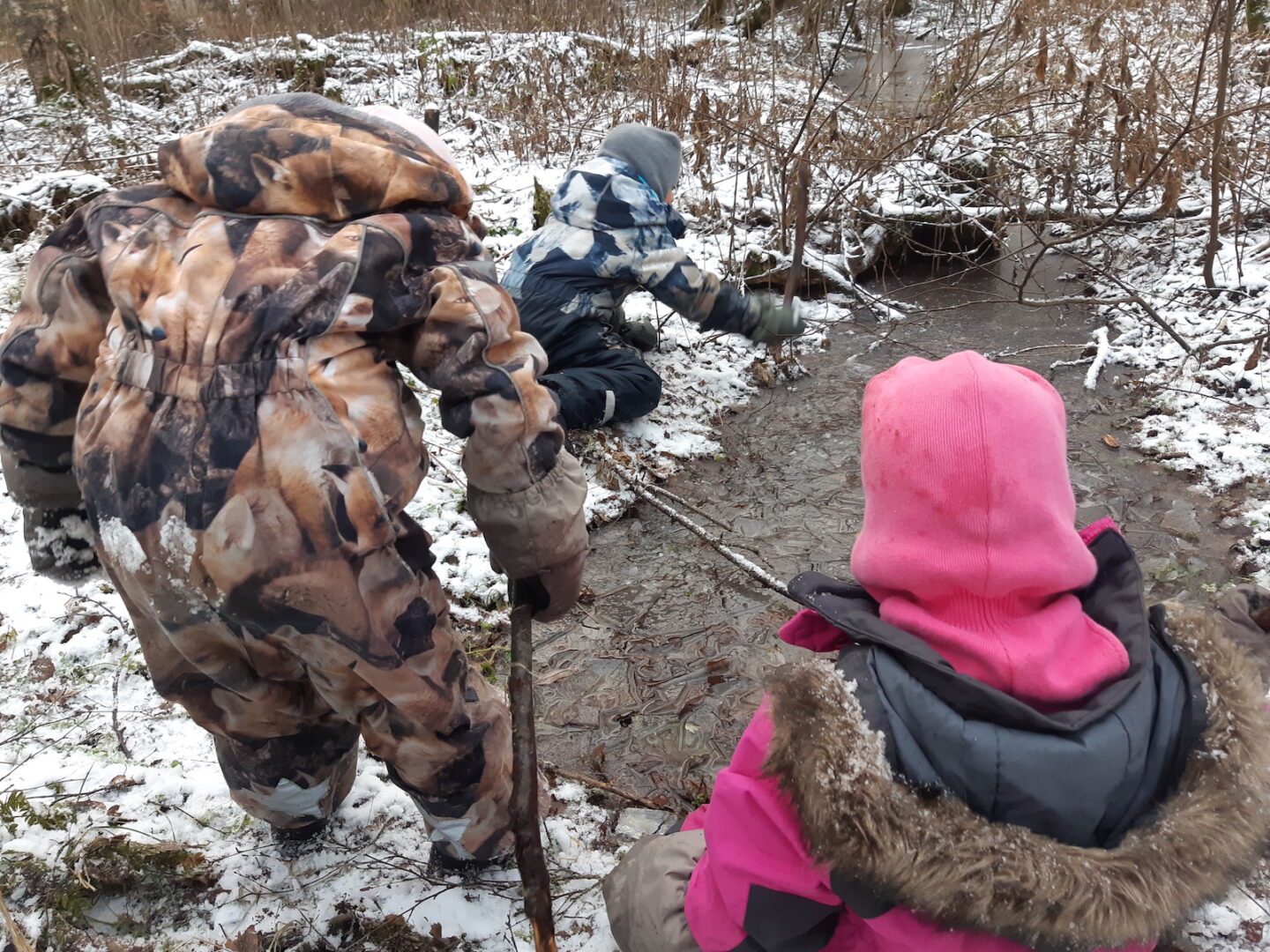 Kolme lasta metsässä rikkomassa jäätä.