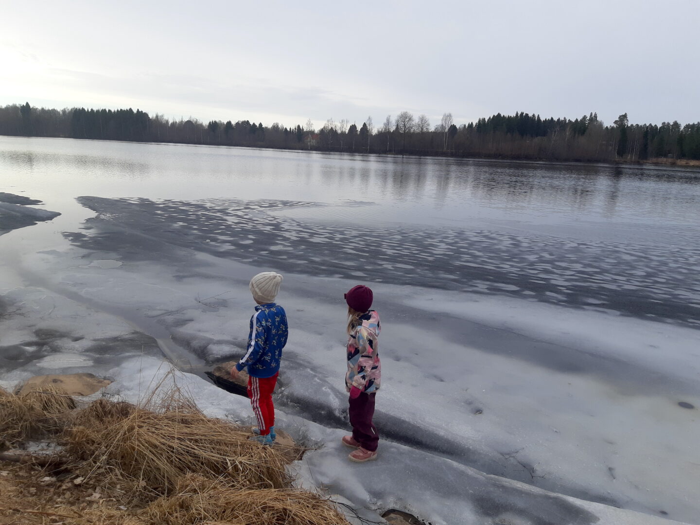 Kaksi lasta joen rannalla jäiden päällä.